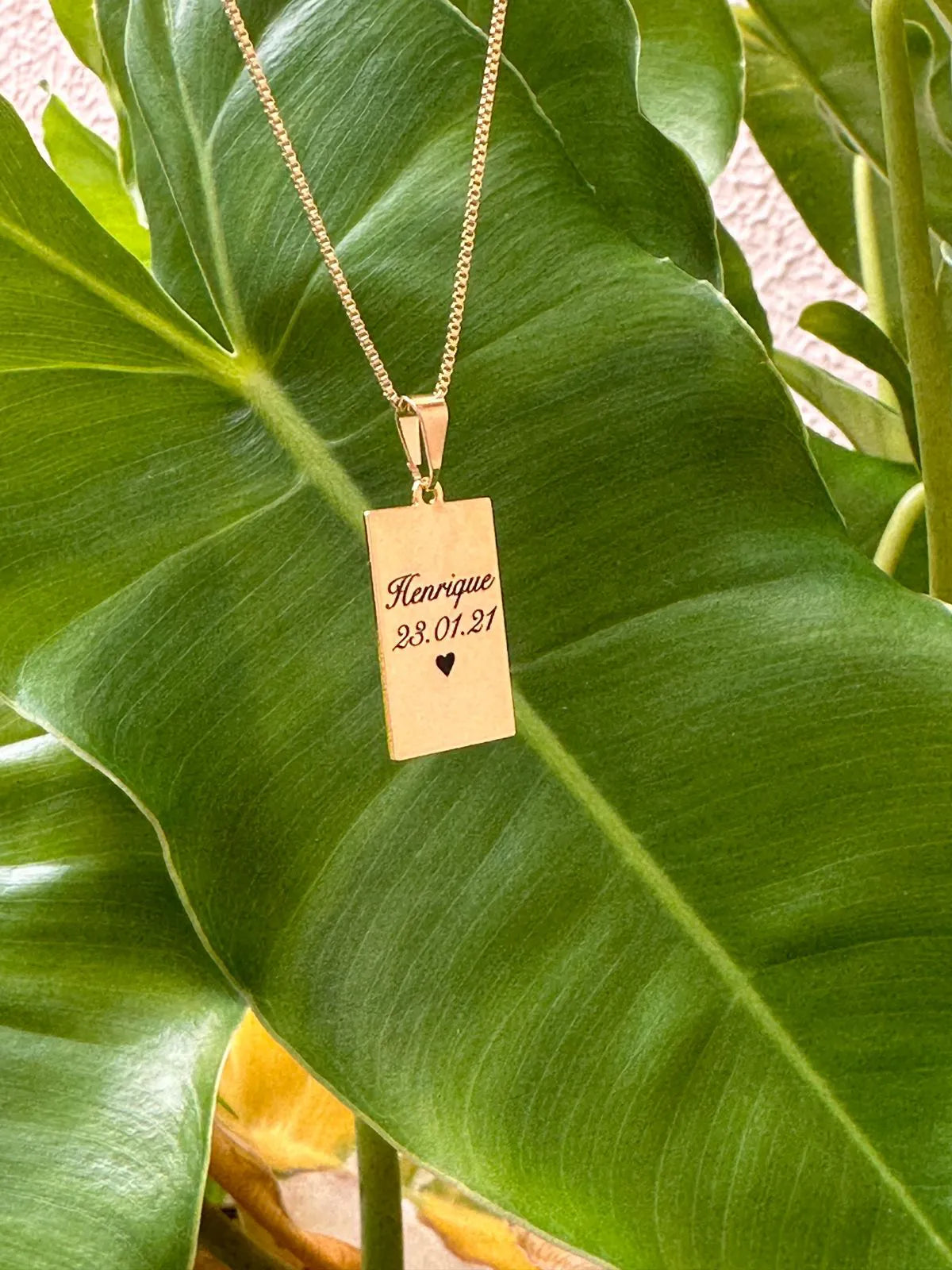 Colar com placa personalizada sobre fundo natural verde - gravação de momentos especiais
